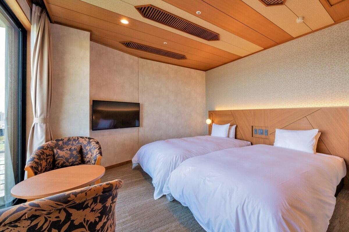 A hotel room with two beds, a flat-screen TV, a small table, and a chair.