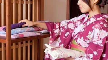 A person in a traditional kimono arranging folded textiles on a wooden shelf.