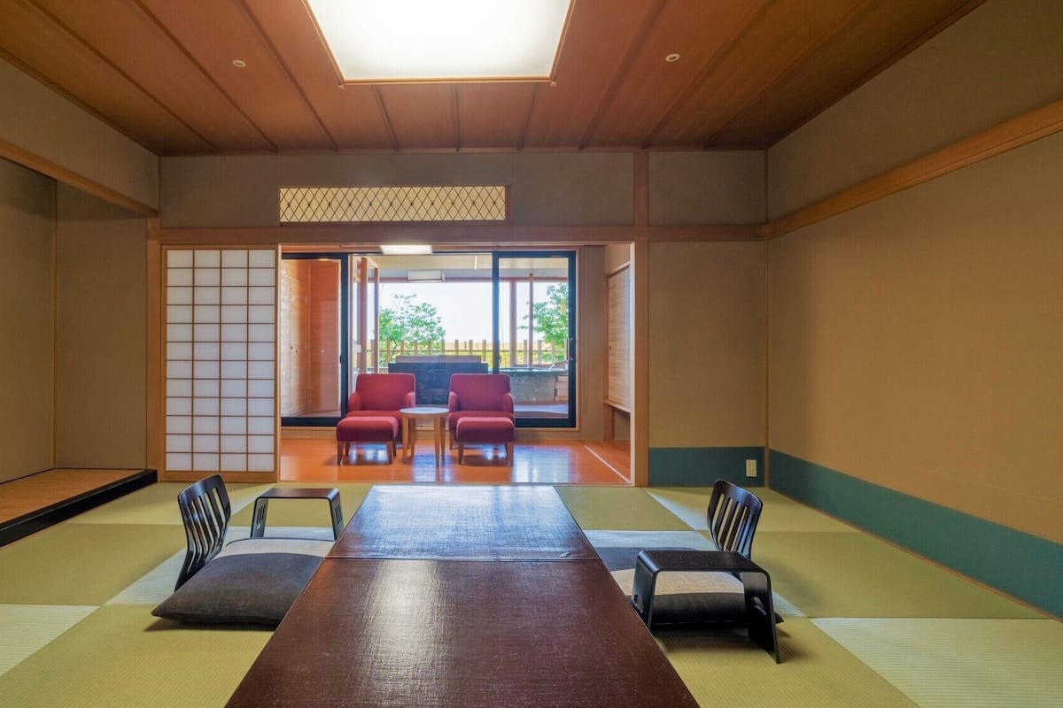A traditional Japanese room with tatami flooring, a low table, and red chairs.