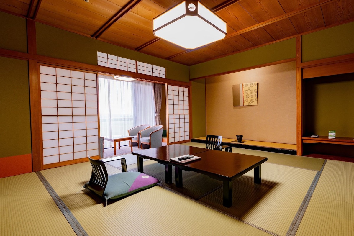 Une pièce de style japonais traditionnel, avec un sol recouvert de tatamis, une table basse, des chaises et une porte coulissante.