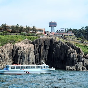Un bote sobre aguas tranquilas cerca de una costa rocosa con edificios al fondo.