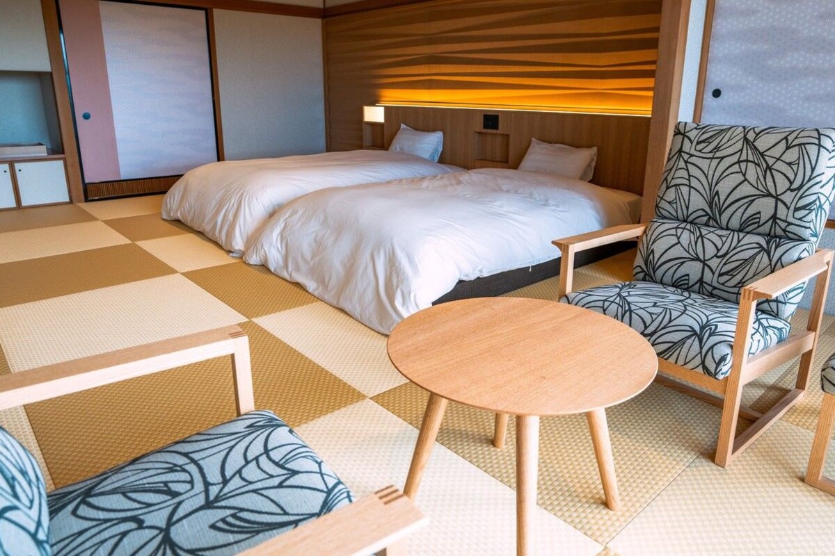 A hotel room with a bed, two chairs, a small table, and a wardrobe.