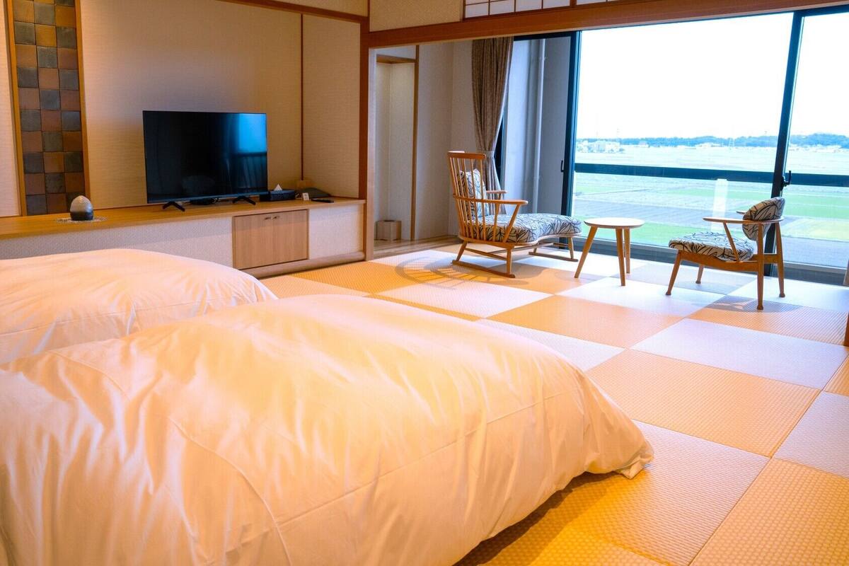 A hotel room with two beds, a TV, a desk, and a view of the water.