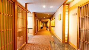 A hotel hallway with traditional wooden sliding doors, a patterned carpet, and a series of framed pictures on the walls.