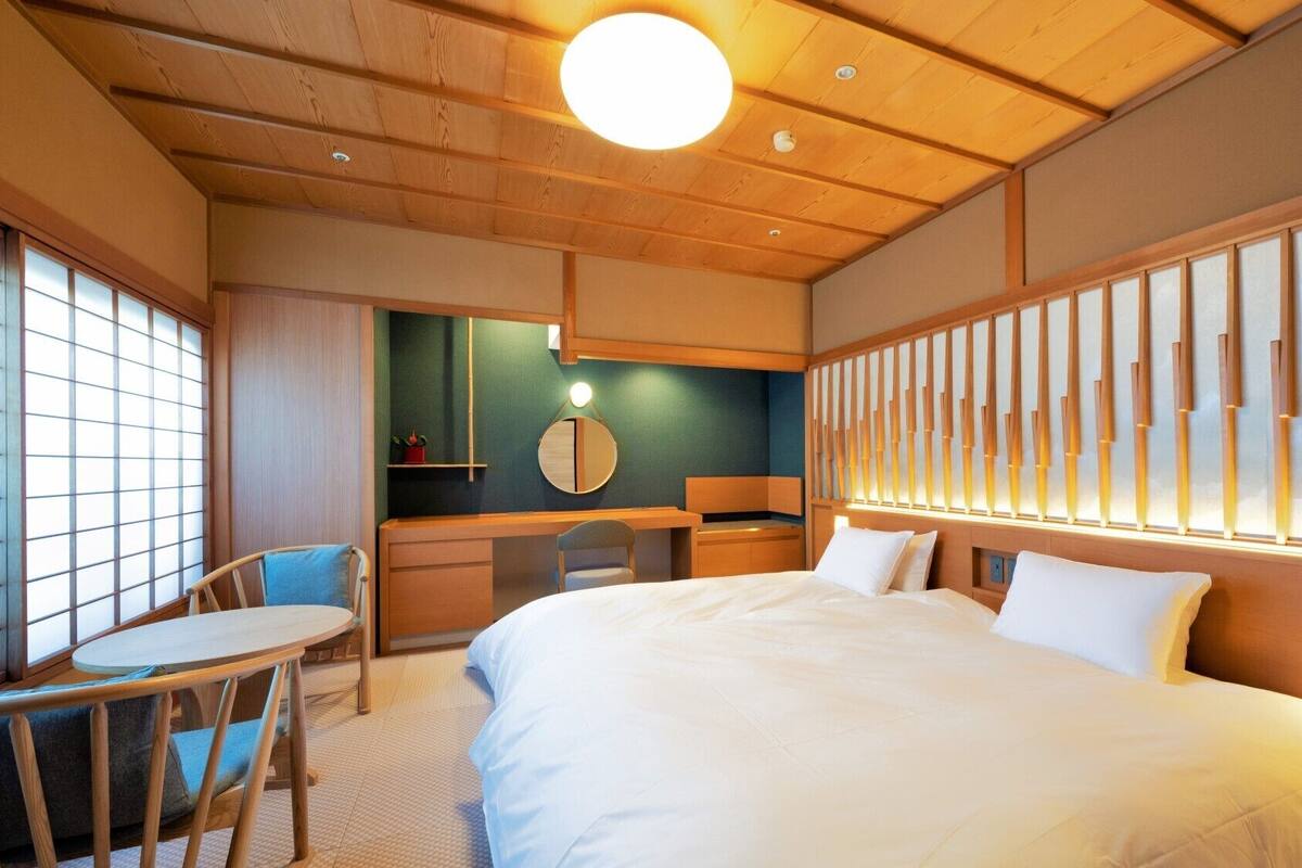 A hotel room with a bed, a desk, a chair, and a wall with vertical wooden slats.