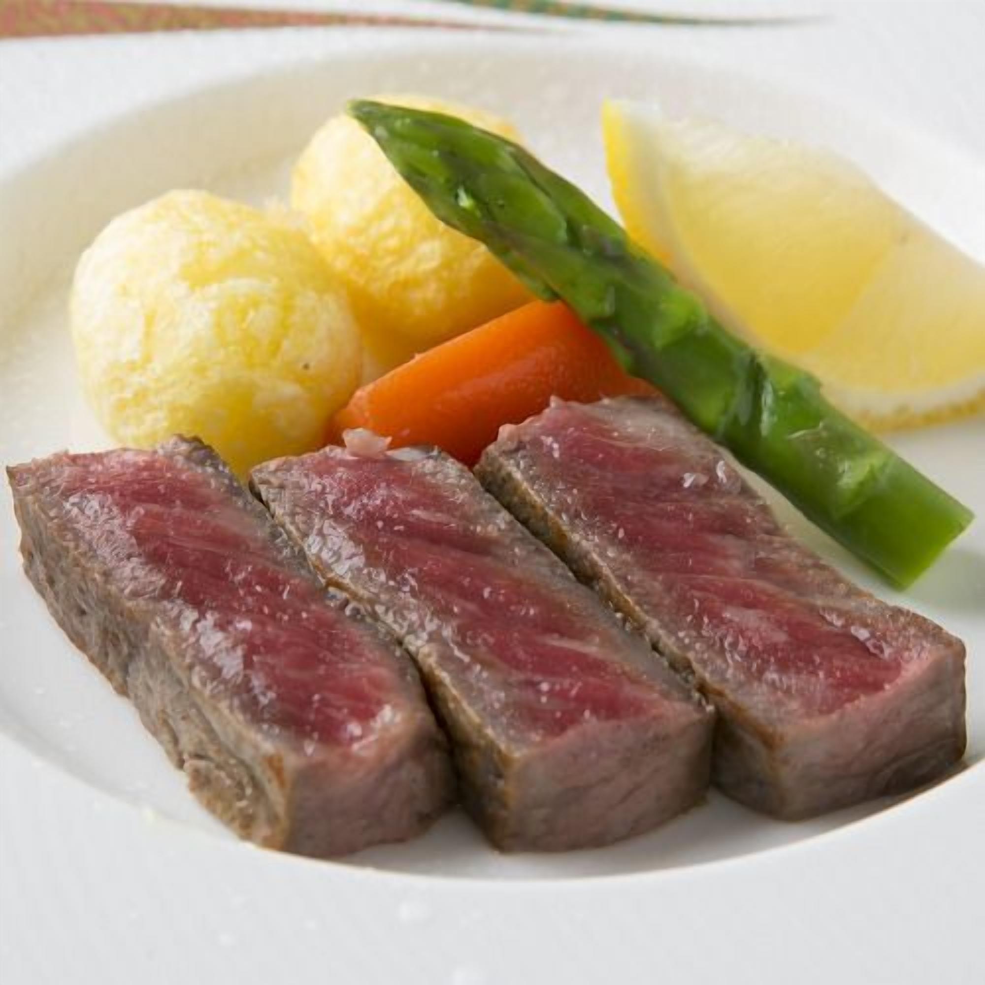 A plate with sliced meat, vegetables, and a lemon wedge.