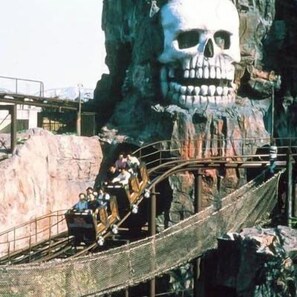 Una vía de montaña rusa con una gran estructura de calavera al fondo.