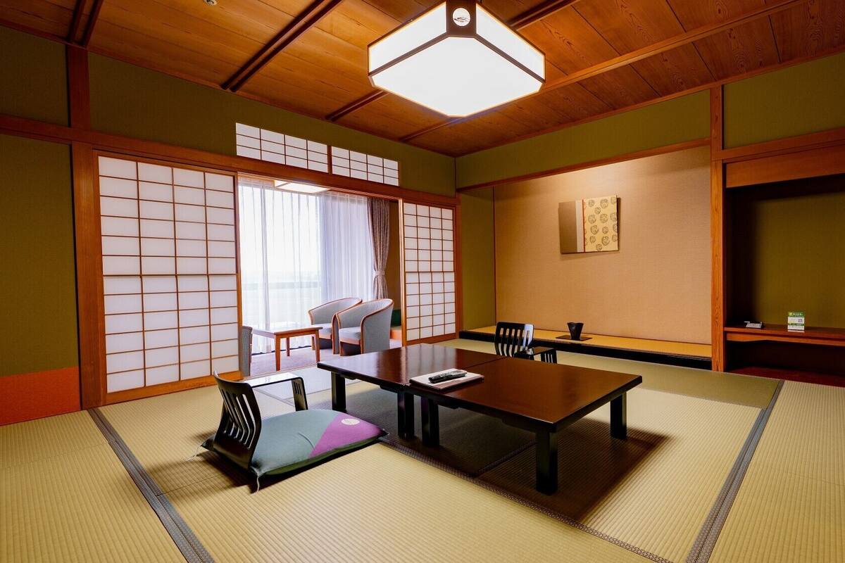 A traditional Japanese-style room with tatami flooring, a low table, chairs, and a sliding door.