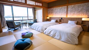A hotel room with two beds, a sitting area with a table and chairs, tatami mats, and a view through large windows.
