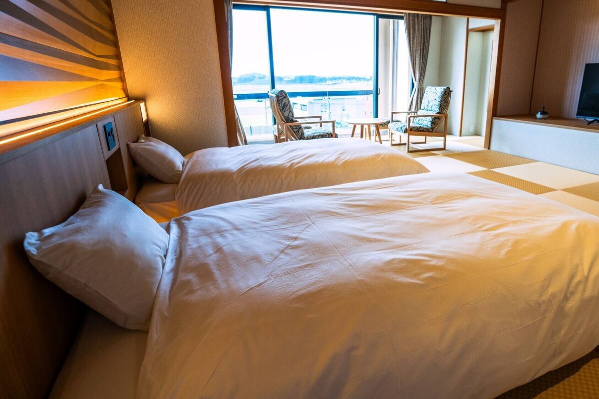 A hotel room with two beds, a TV, and a view of the sea.