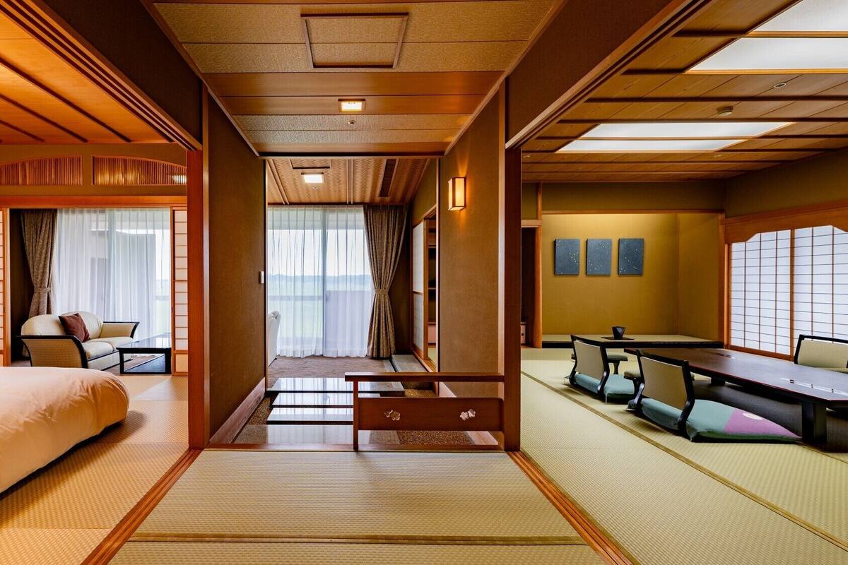 A traditional Japanese-style hotel room with tatami flooring, a bed, a sofa, a dining table, and sliding doors.