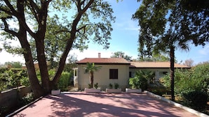 A two-story house with a red-tiled roof, surrounded by trees and a paved driveway. - Holiday apartment with balcony (Njivice)