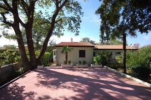 Una casa a due piani con tetto in tegole rosse, circondata da alberi e un vialetto lastricato.