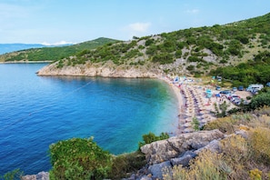Una spiaggia costiera con acque blu cristalline, scogliere rocciose e vegetazione lussureggiante.