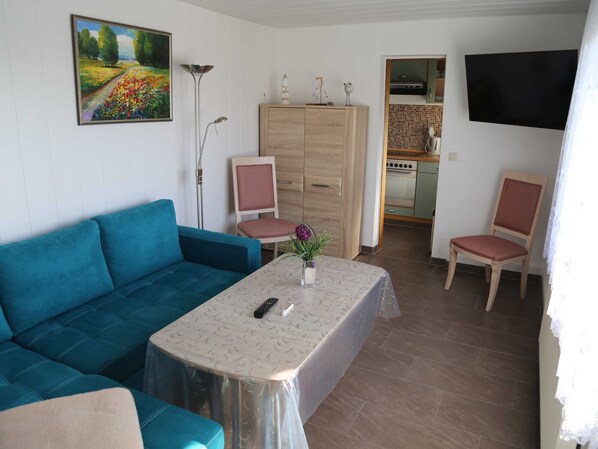 Una sala de estar con un sofá azul, una mesita con un jarrón, un mueble de madera y una cocina al fondo.
