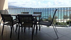 A balcony with a table and chairs overlooking a coastal view.