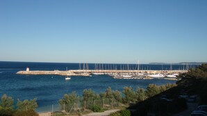 A marina with multiple sailboats docked, a lighthouse, and a clear blue sky.