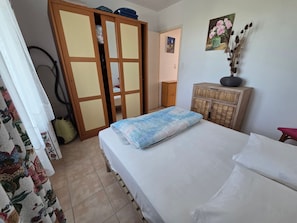 A bedroom with a bed, a wardrobe, a small cabinet, and a painting on the wall.