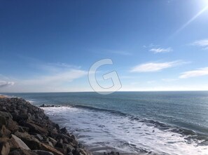Un paysage côtier avec une rive rocheuse et une mer calme sous un ciel dégagé.