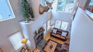 Un salon aux hauts plafonds, orné d’une tête de cerf accrochée au mur, avec une cheminée, un canapé en cuir marron et une table basse.
