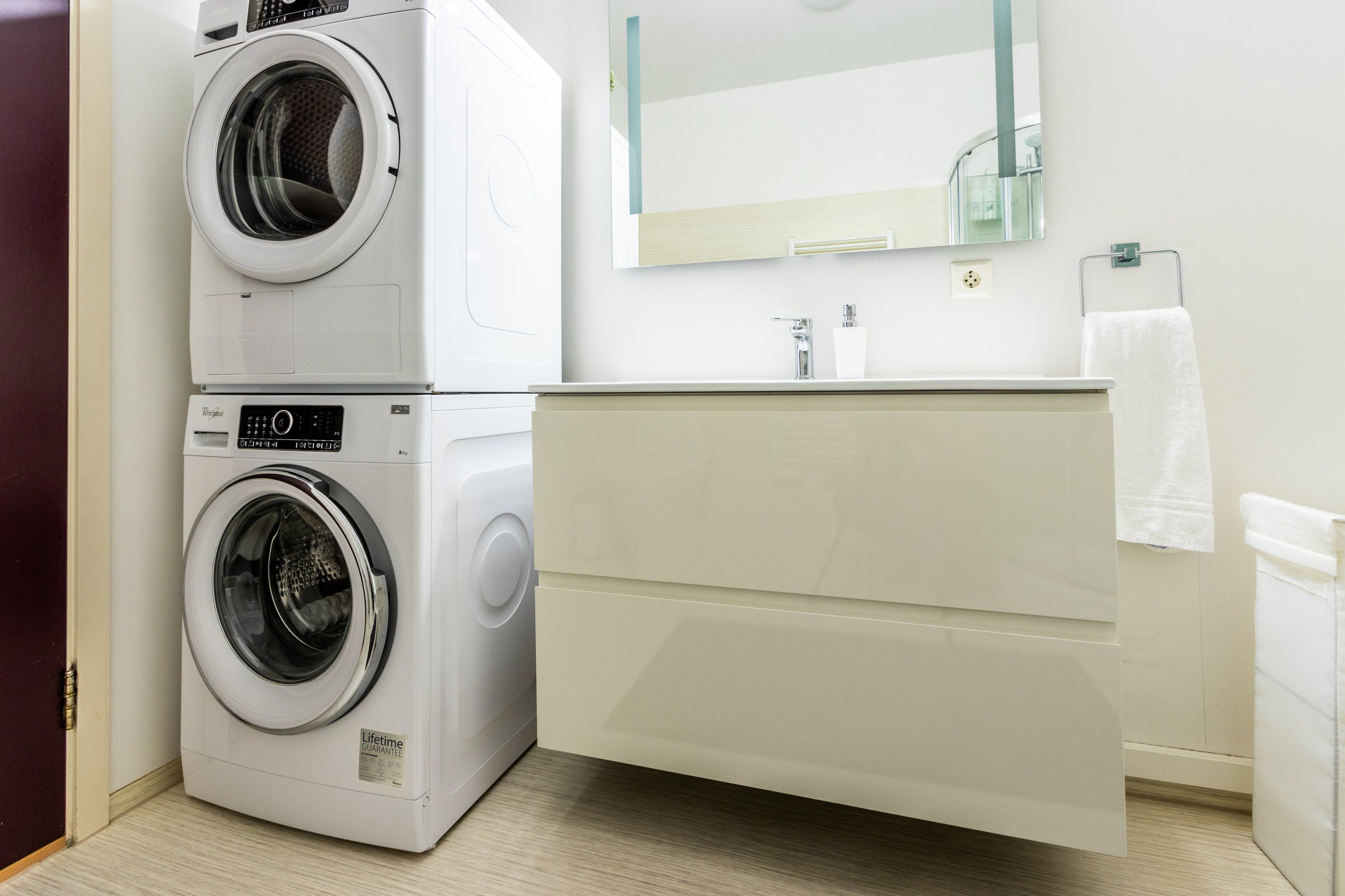 Un baño compacto con lavadora y secadora apiladas, un lavamanos moderno y un espejo sobre el mueble de tocador.