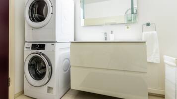 Un baño compacto con lavadora y secadora apiladas, un lavamanos moderno y un espejo sobre el mueble de tocador.