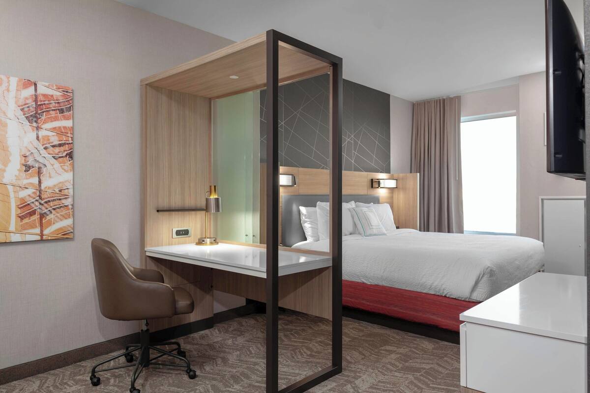 Una camera d'albergo con un letto, una scrivania con una sedia, una televisione e un quadro appeso al muro.