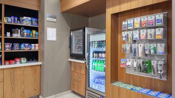 A small market area with shelves stocked with snacks and beverages, a refrigerator with drinks, and a display of toiletries.