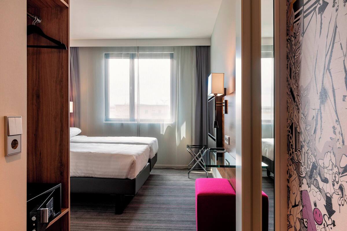A hotel room with a bed, a desk, a chair, and a window with curtains.