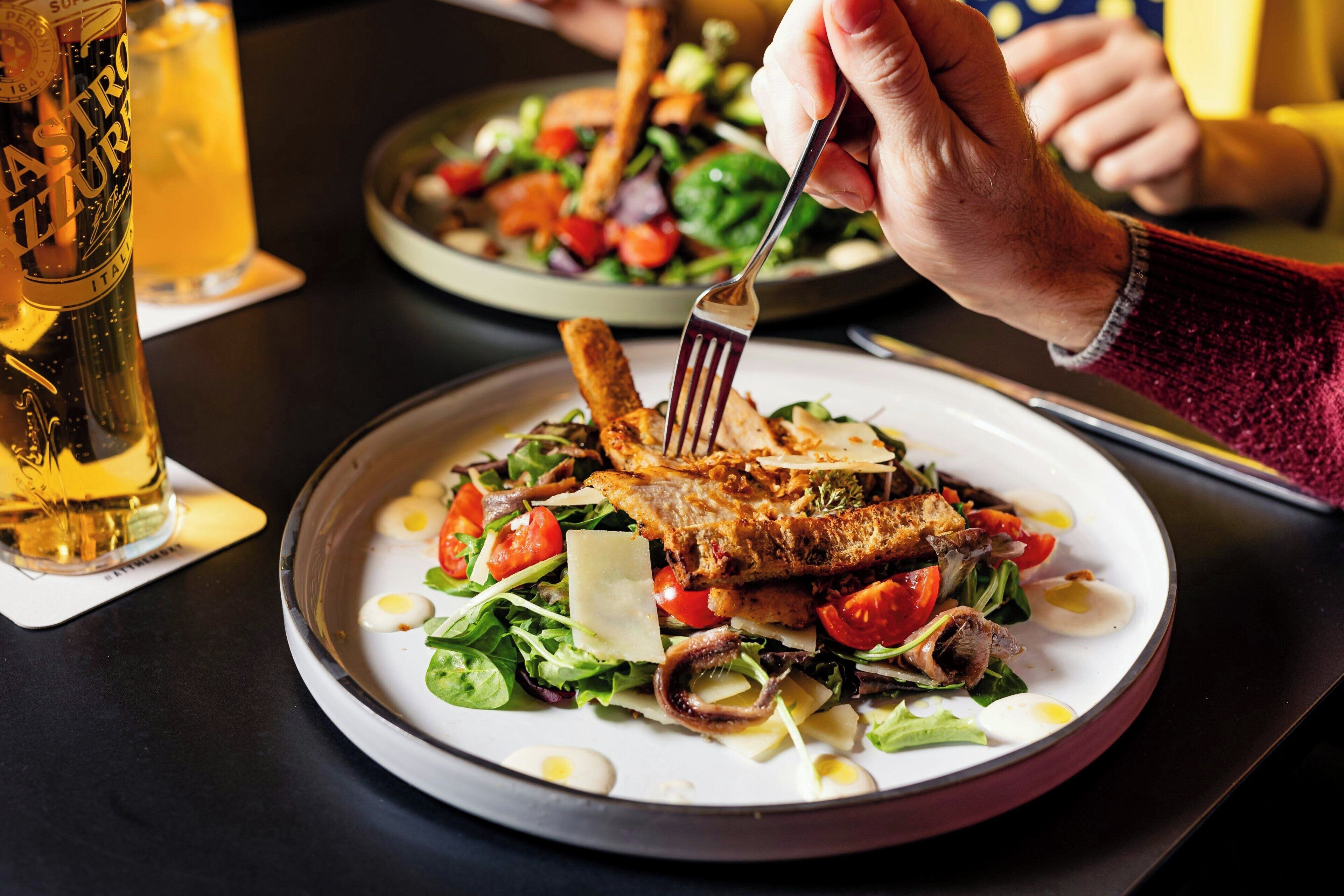 Une table à manger avec une assiette de nourriture, un verre de bière et une bouteille de bière.