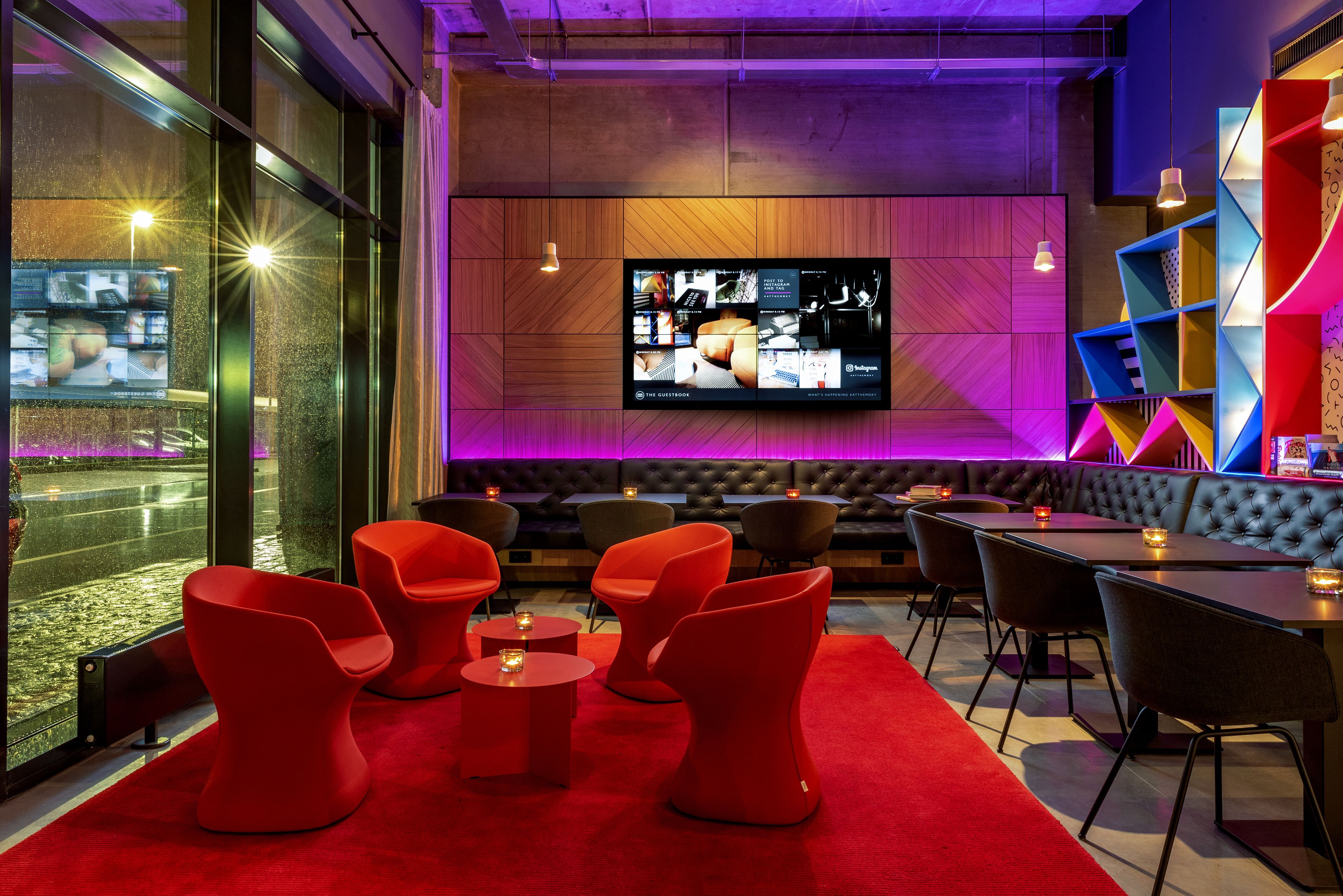 A modern bar area with red chairs, a large TV screen, and a wooden wall.