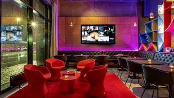 A modern bar area with red chairs, a large TV screen, and a wooden wall.