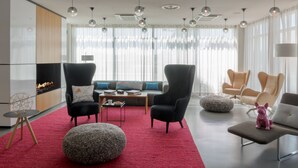 A modern living room with a red carpet, black and beige chairs, a round ottoman, and a small pink dog statue. - Moxy Milan Linate Airport (Segrate)