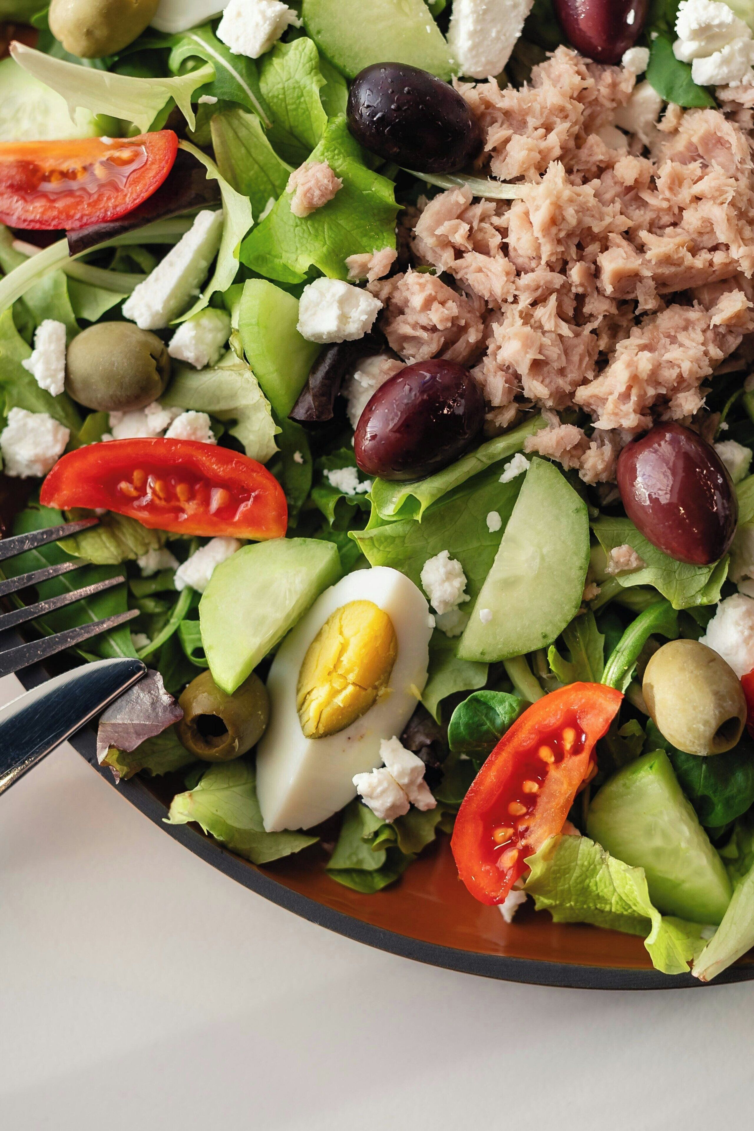 Ein Salat mit verschiedenen Zutaten, darunter Blattsalat, Tomaten, Oliven und ein hartgekochtes Ei.
