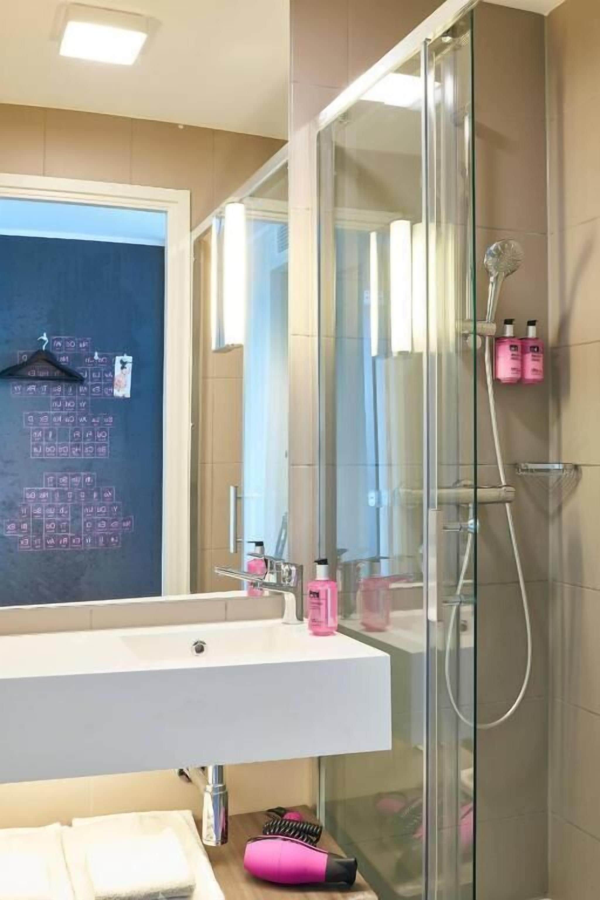 A modern bathroom with a glass shower enclosure, a white sink, and a mirror.