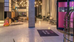 A modern interior with geometric ceiling design, seating areas, and a reception desk. - Moxy Milan Linate Airport (Segrate)