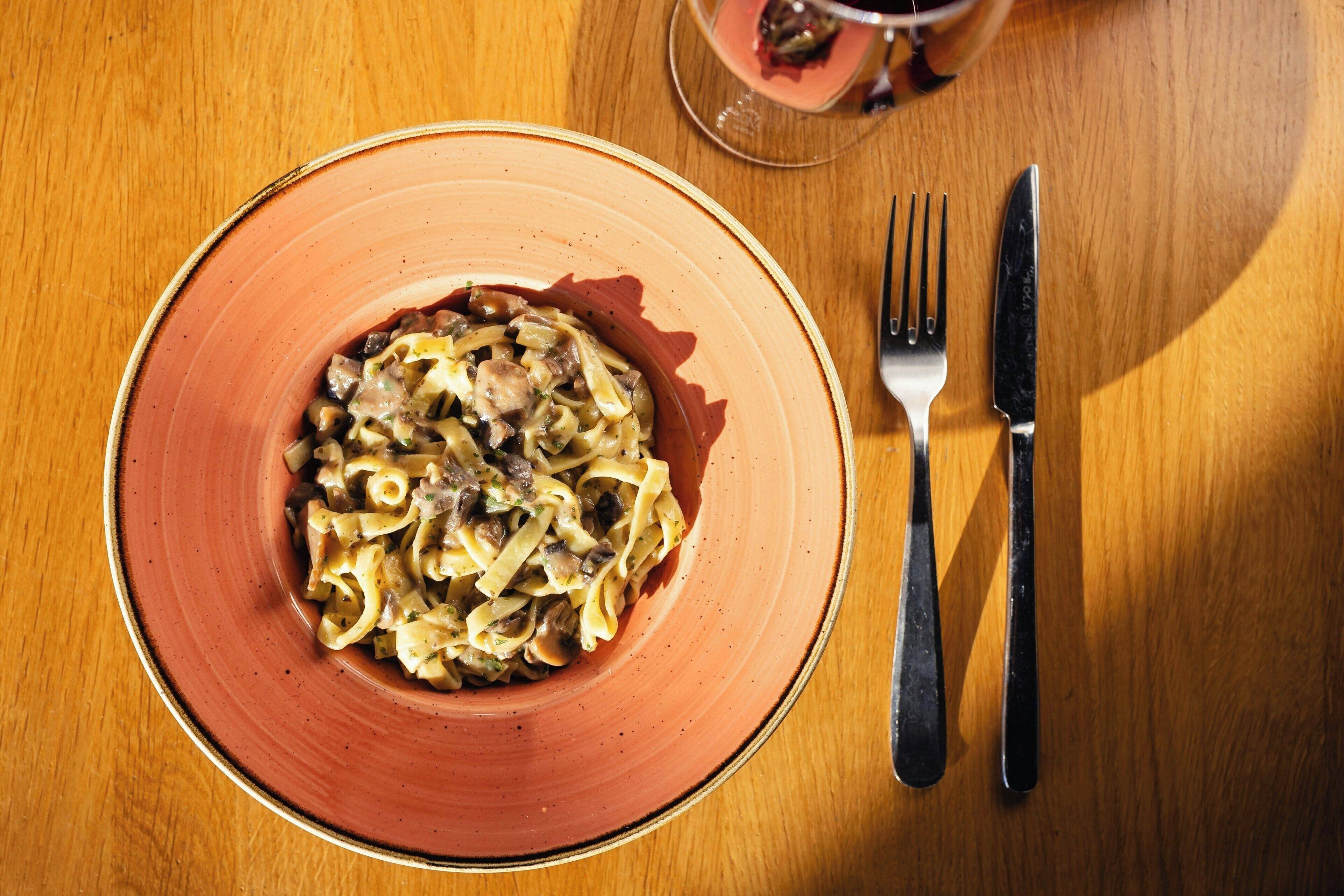 Un piatto di pasta con forchetta e coltello su un tavolo di legno.