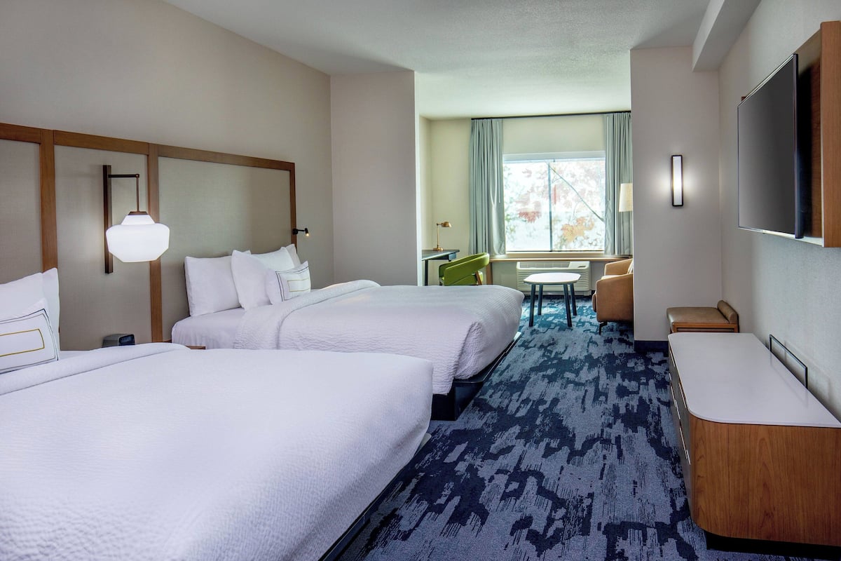 A hotel room with two beds, a desk, a chair, a TV, and a window with curtains.