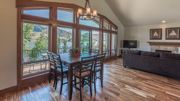 A spacious room with a dining table and chairs, a sofa, and large windows offering a view of greenery and mountains. - Wapato Lake Retreat-Sleeps 6, Waterfront and dock! (Manson)