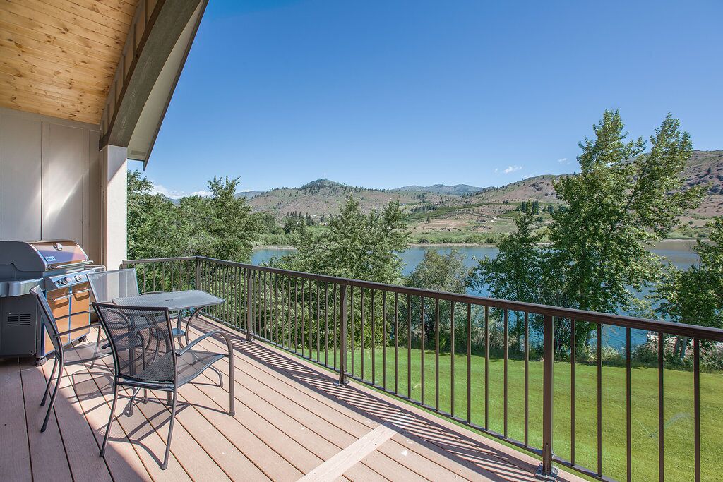 Un balcón con una parrilla, mesa y sillas con vista a un lago y colinas.