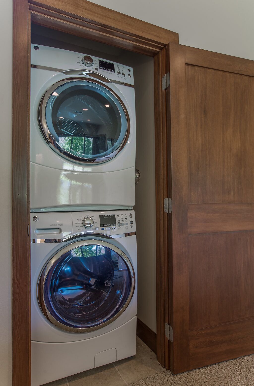 A stacked washer and dryer unit in a corner with a wooden door.