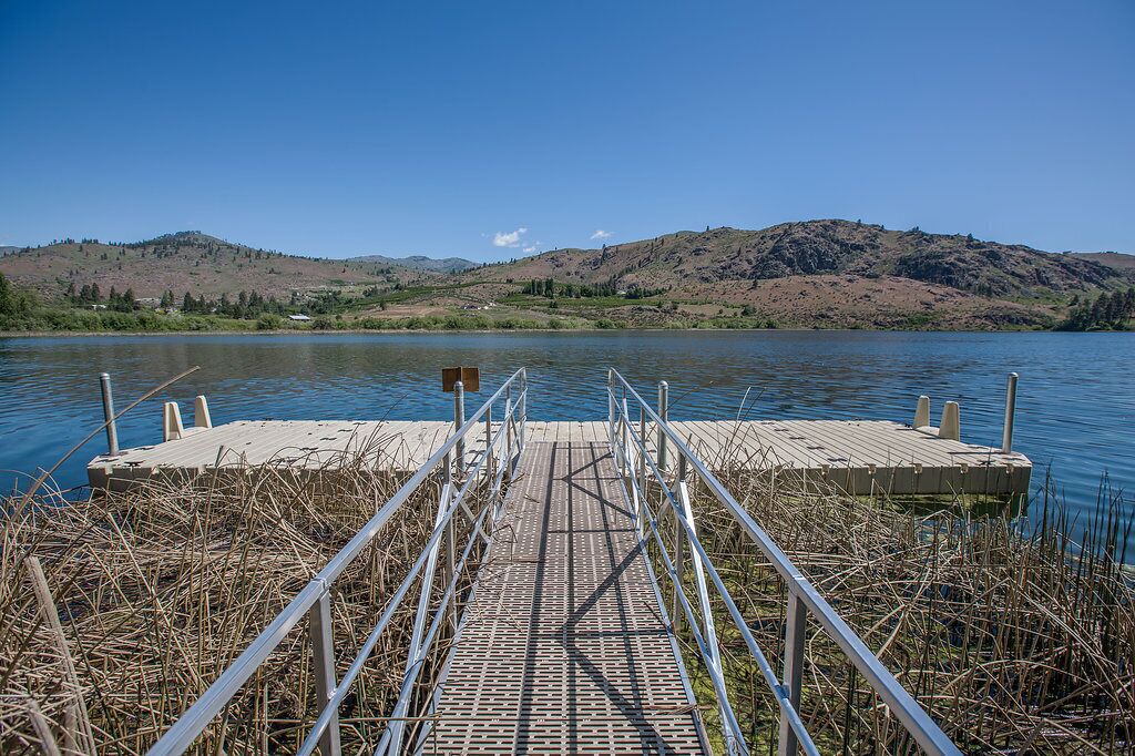 A wooden dock extending into a calm lake with a hilly landscape in the background.