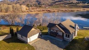 A house with a garage and a porch, surrounded by a lake and mountains. - Wapato Lake Retreat-Sleeps 6, Waterfront and dock! (Manson)