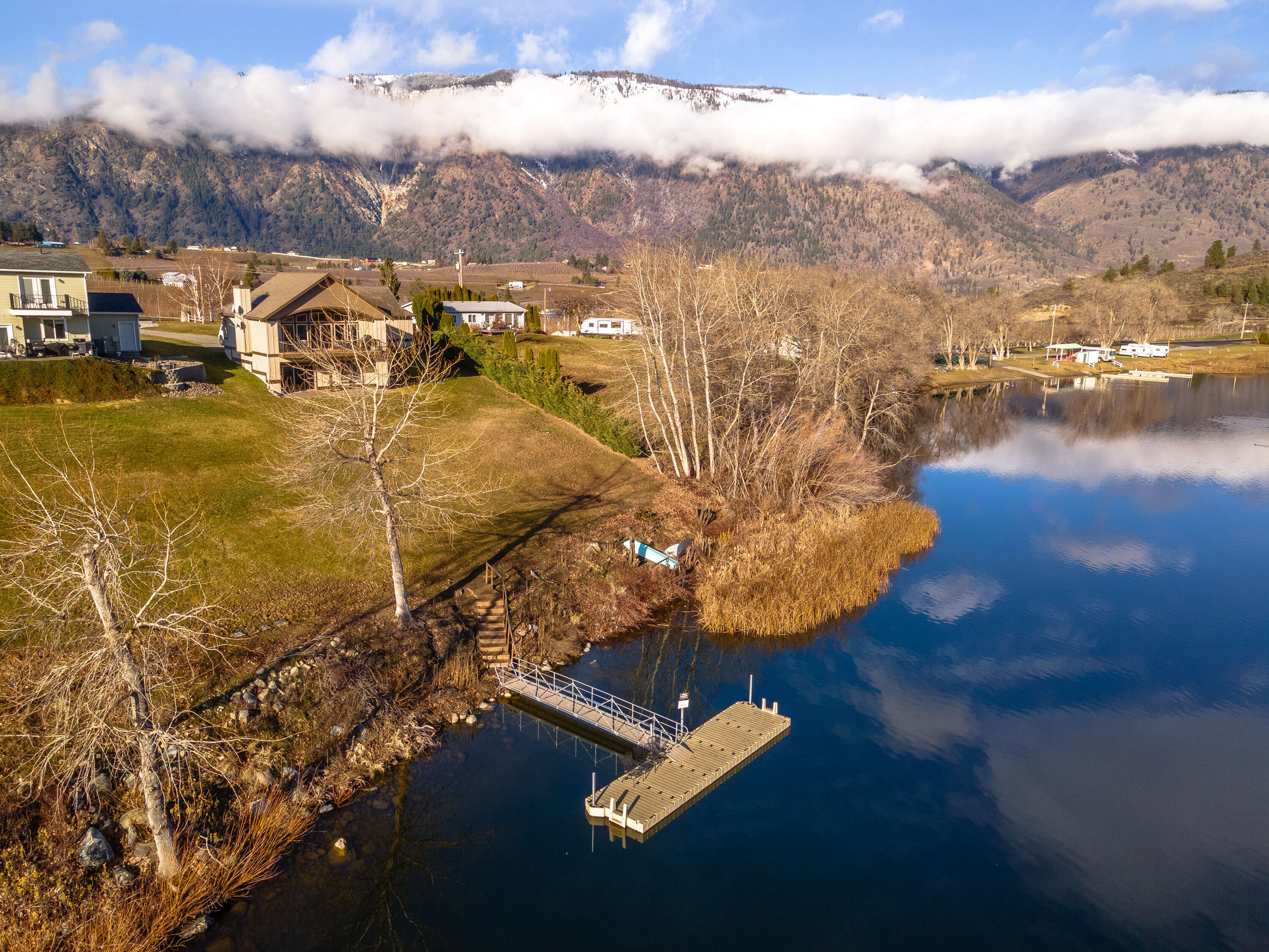 A lakeside property with a dock, a house, and a mountain backdrop.
