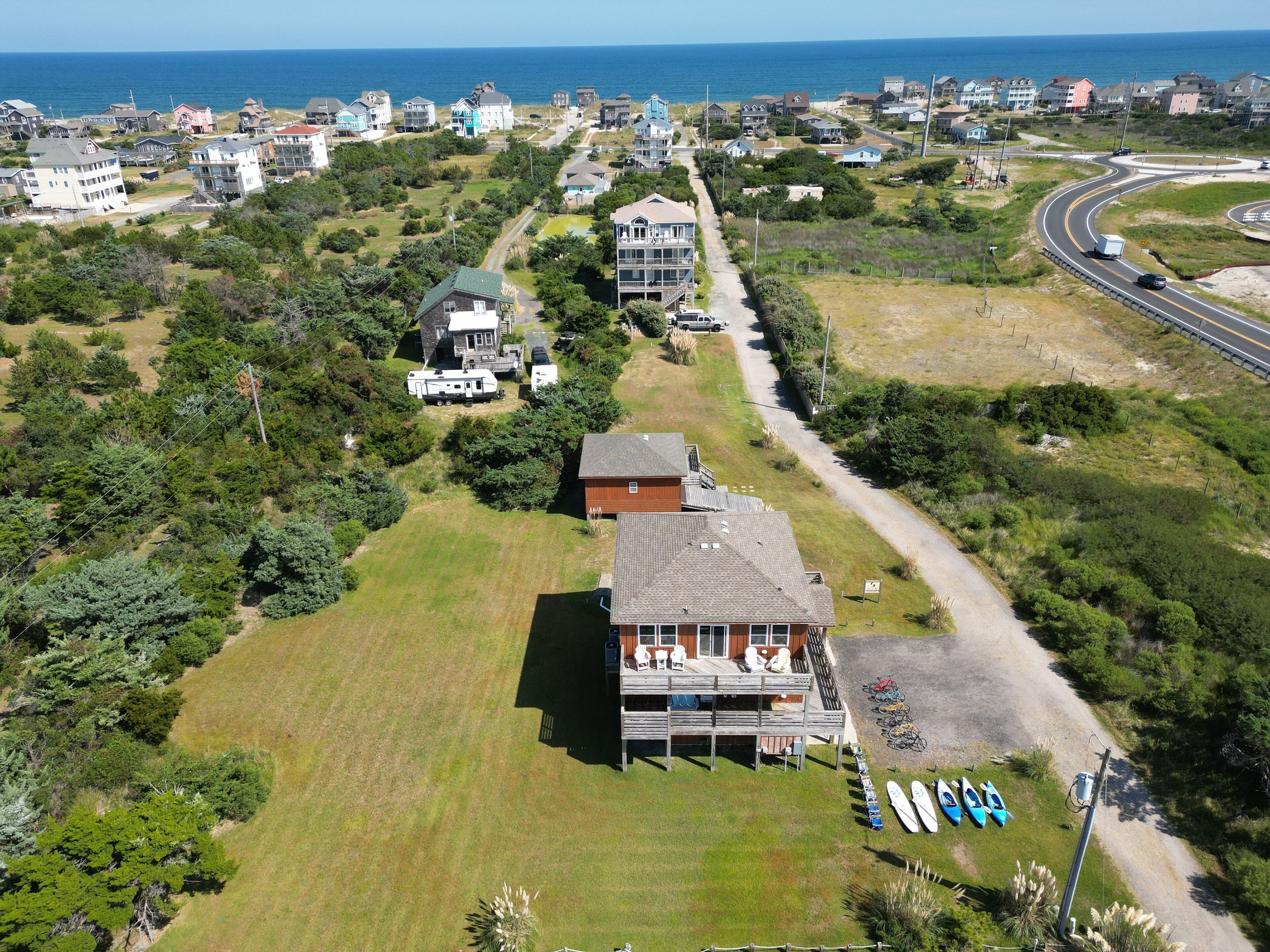 An aerial view of a coastal residential area with houses, a road, and a beach.
