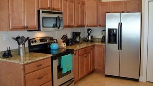 A kitchen with wooden cabinets, a stainless steel refrigerator, a microwave, an oven, and a coffee maker. - OBX Beach House + Bikes-Paddle Boards-Kayaks-Beach Chairs-Great Fishing! (Rodanthe)