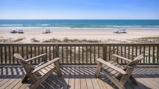 A wooden deck with two chairs overlooking a beach with umbrellas and lounge chairs.