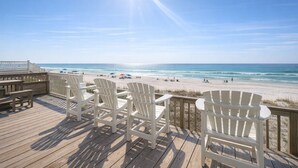 A wooden deck with white chairs overlooking a beach.