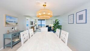 Un espace repas avec une longue table et des chaises, un lustre et des œuvres d’art encadrées accrochées aux murs.
