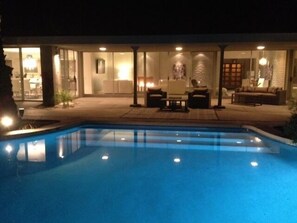 En swimmingpool med en uteplats, utomhusmöbler och ett väl upplyst inomhusområde.